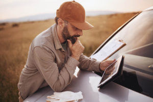 A white, bearded man uses a tablet in a rural field