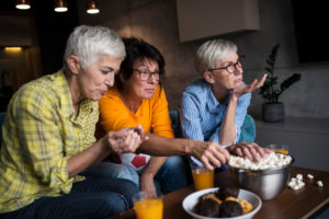 Senior women eating popcorn and macarons while watching Buckeye Broadband TV on the couch