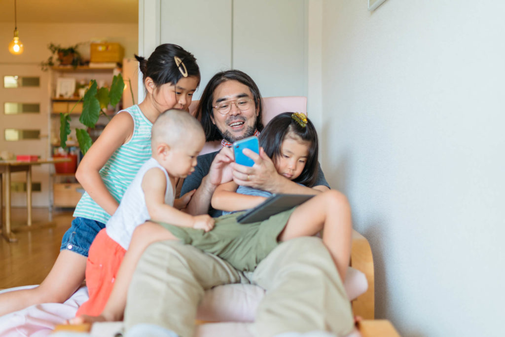 Man sitting on the floor with three children, all of them looking at smartphone