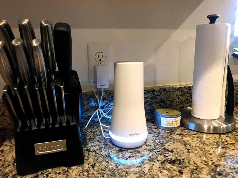 SimpliSafe base station shown on a granite countertop in between a kitchen knife block and a paper towel holder