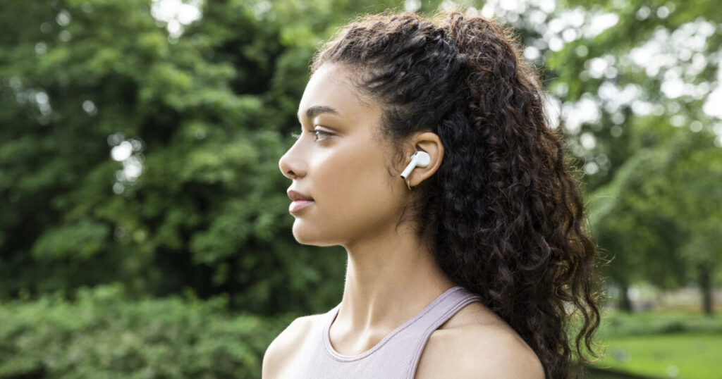 Young woman with curly dark hair wearing Belkin SOUNDFORM wireless earbuds outdoors