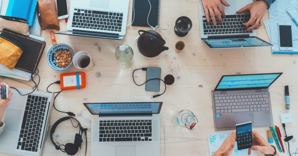 overhead shot of five laptops on a table with coffee and phones