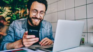 man on laptop using phone and laughing