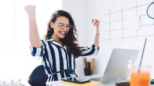 Excited woman in striped dress smiling at laptop