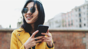 woman wearing sunglasses and yellow jacket holding phone and smiling