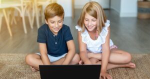 two kids sitting together and playing on a laptop computer