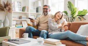 happy couple sitting on couch in trendy room surrounded by plants while watching tv