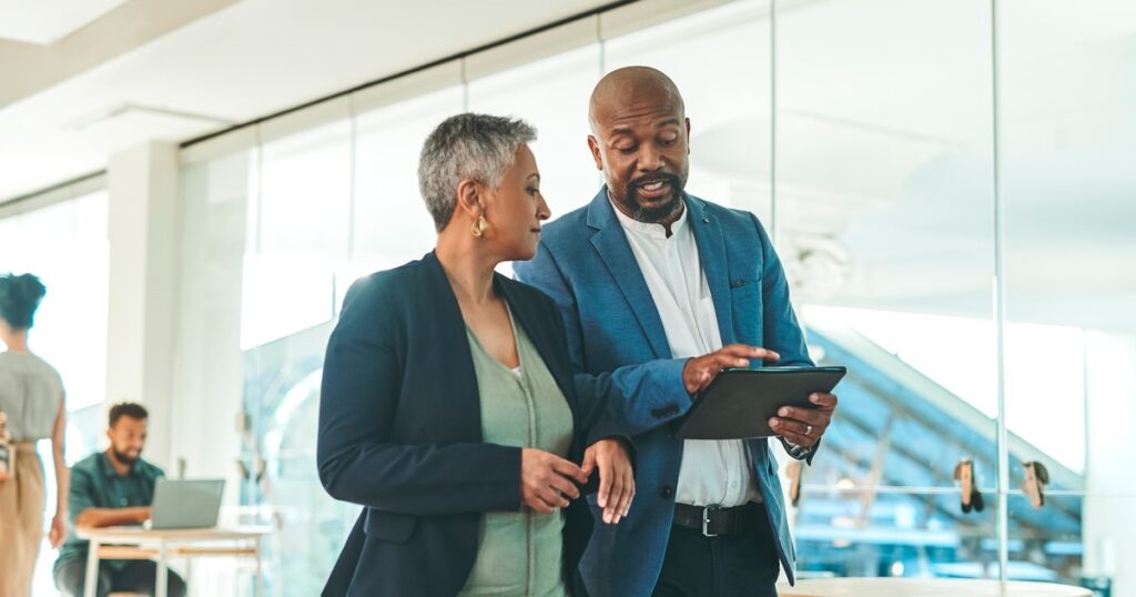 a woman and a man in business attire standing and looking at a tablet