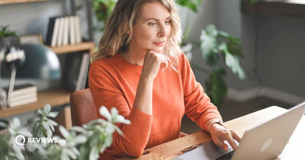 woman in orange sweater using laptop