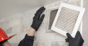 dirty aircon duct being taken off the wall by black gloved hands