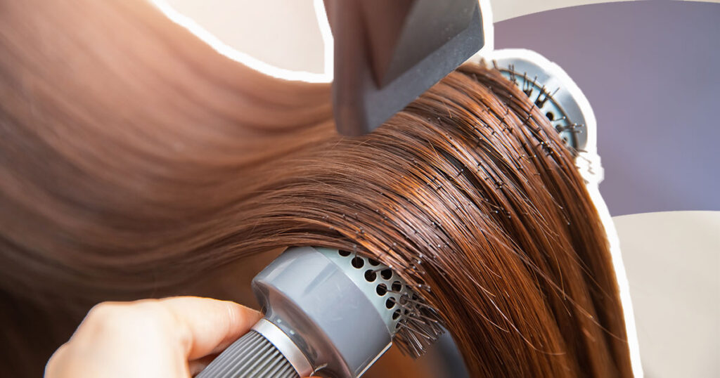 hair dryer concentrator on round brush, combing through long, straight brown hair
