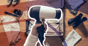 hair dryer being held above a suitcase, with items to be packed scattered around