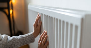 hands touching a gas heater gently like the small amount of warmth is the only thing grounding the person to the planet