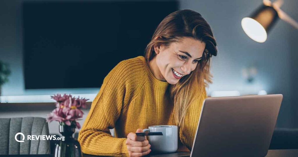 Woman smiling at a laptop screen while holding a mug