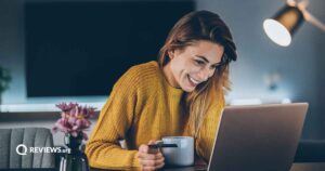 Woman smiling at a laptop screen while holding a mug