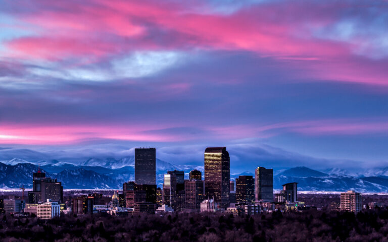 Photography of the Denver Skyline at Sunset with snowy winter peaks in distance.