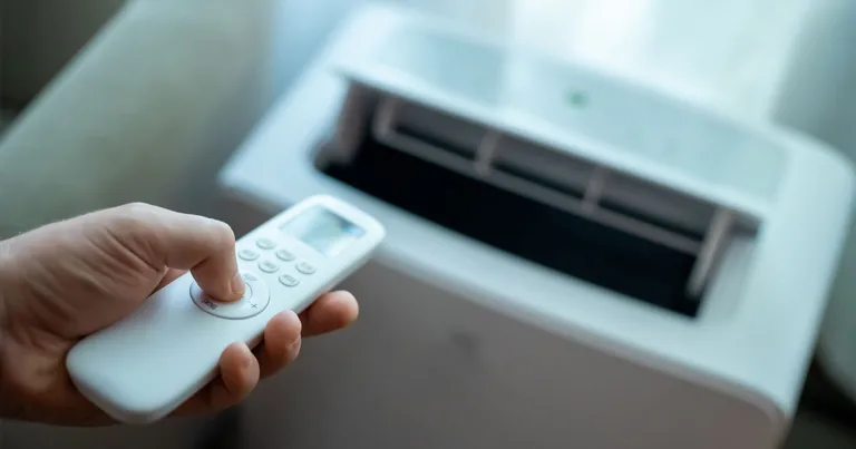 person aiming a remote at a portable air conditioner with open vents